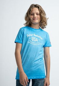 Ljusblå bomulls t-shirt med rund halsringning, korta ärmar och vit tryckt text i mitten. Bärs med strukturerade blå jeans.