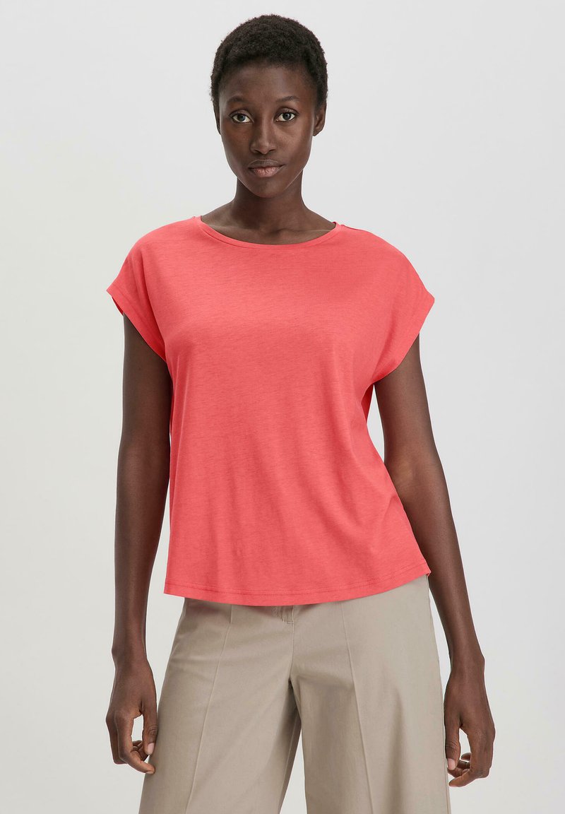 Koraalkleurig T-shirt met korte mouwen, een ronde halslijn en een ontspannen pasvorm, gemaakt van zachte stof, gecombineerd met lichtbeige wijde broek.