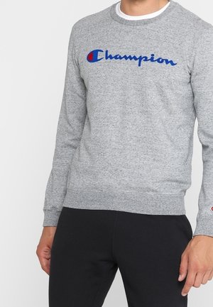 Sudadera gris de mezcla de algodón, con mangas largas, puños acanalados y cuello redondo. Logo azul bordado de "Champion" en el pecho.