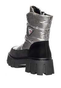 Botte de cheville isolée argentée avec un accent en daim noir, semelle en caoutchouc texturé épais et un patch logo triangulaire près du talon.