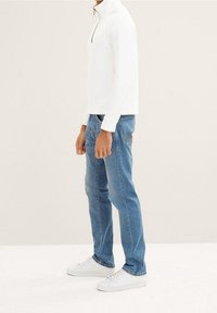 Sudadera blanca con cremallera y cuello alto, combinada con jeans de mezclilla azul claro y zapatillas blancas, mostrando un estilo casual.