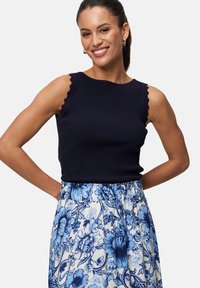 Débardeur en maille côtelée navy avec des bretelles festonnées, associé à une jupe légère à motifs floraux dans des tons de bleu et dotée d'une taille froncée.