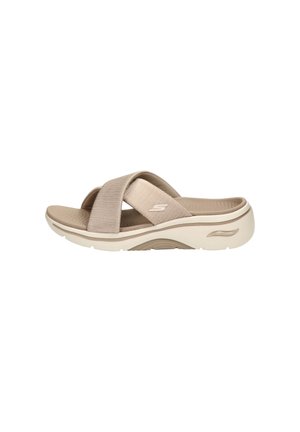 Beige slip-on sandal with two wide fabric cross straps, contoured cushioned sole, and subtle brand logo on side strap.