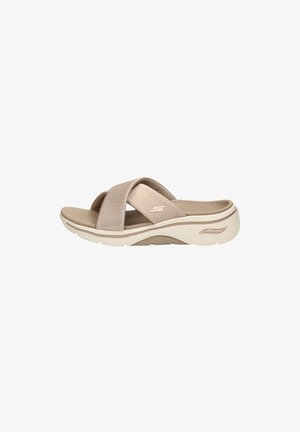 Beige slip-on sandal with two wide fabric cross straps, contoured cushioned sole, and subtle brand logo on side strap.
