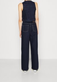 Jeansowa kamizelka i spodnie o szerokich nogawkach w ciemnym granatowym kolorze. Kamizelka ma dopasowany krój, natomiast spodnie są luźne, z tylnymi kieszeniami i kontrastowym przeszyciem.