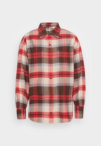 Chemise en flanelle à carreaux rouge et marron avec manches longues, fermeture à boutons et deux poches à la poitrine ; présente des motifs à carreaux variés et une texture douce.