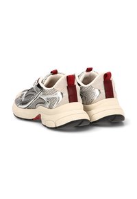 Zapatillas deportivas con parte superior de malla metálica plateada, detalles en ante beige y tiradores rojos. Suela gruesa color crema con suela exterior negra.