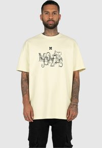 Light yellow cotton t-shirt with a relaxed fit, featuring a black graphic design in various fonts on the front. Short sleeves, crew neckline.