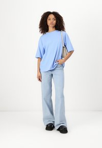 Ljust blå oversized t-shirt med korta ärmar, ihopparad med ljusblå utsvängda jeans. Modellen håller en liten grå väska och bär svarta platåskor.