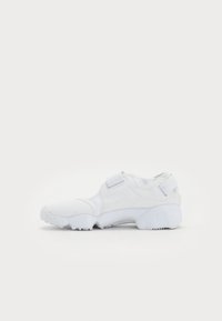 White athletic shoe with a sock-like design, featuring a hook-and-loop strap and textured fabric. Molded rubber outsole for traction.