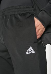 Black athletic pants with a smooth finish, elastic waistband, zippered pocket, and a white Adidas logo near the hem.