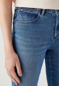 Slim-fit blå denimjeans med en lätt blekning, med hög midja, fem fickor och metalldetaljer. Mjuk textur, blandning av bomull.