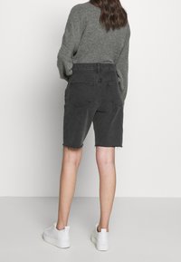 Mustat farkkushortsit, joissa on revitty helma, korkea vyötärö ja takataskut, yhdistettynä harmaaseen villapaitaan ja valkoisiin tennareihin.