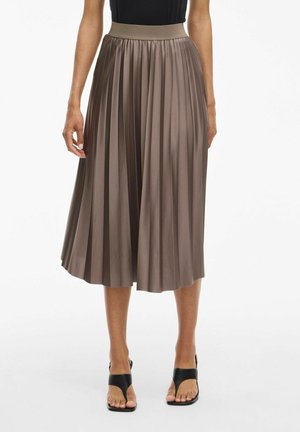 Jupe midi plissée taupe portée avec un haut noir et des sandales à talons ouvertes noires sur une personne debout sur fond blanc.