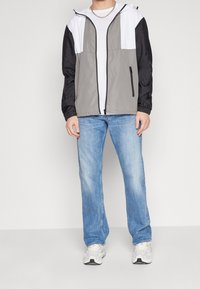 Chaqueta de rompevientos ligera en bloques de color gris, negro y blanco, con cierre de cremallera, capucha ajustable y bolsillos laterales.