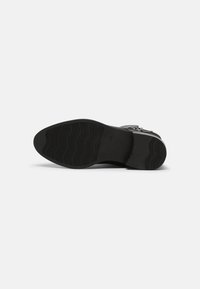 Semelle d'une chaussure habillée noire montrant une semelle en caoutchouc texturée avec un petit talon sur fond blanc.