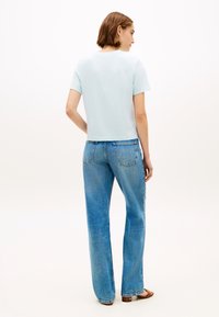 T-shirt en coton bleu clair avec une coupe ajustée, associée à un jean en denim bleu taille haute, à jambes larges et au style classique à cinq poches.