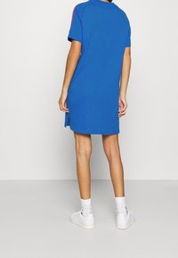 Modré šaty s krátkým rukávem a volným střihem, s kulatým výstřihem a bočními rozparky. Nošeny s bílými teniskami a ponožkami.