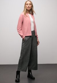 Světle růžová bomber bunda přes bílý top, se šedými širokými kalhotami s texturou a černými kotníkovými botami. Jednoduchý, moderní design s kapsami.