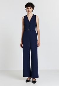 Combinaison navy avec un haut de gilet ajusté comportant trois boutons, un pantalon à jambe large et une texture de tissu lisse.