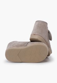 Pantofole per bambino morbide beige con tessuto a coste e suole in gomma, una pantofola mostra il motivo della suola di taglia 21.