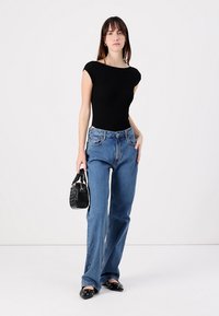Black fitted top, blue flared jeans, and black textured handbag. The outfit features a simple design and flat shoes with a rounded toe.