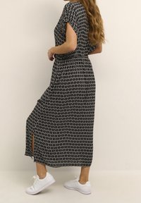 Vestido maxí de estampado en blanco y negro con mangas cortas, cintura elástica y abertura lateral, combinado con zapatillas blancas. Textura de tejido suave.