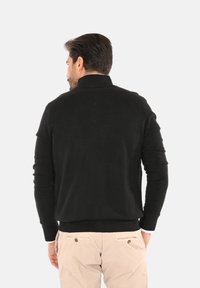 Maglione nero con colletto alto, design aderente e maniche lunghe. Tessuto a maglia, finitura liscia e orlo a coste. Visualizzazione dal retro.