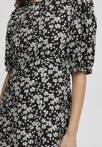 Robe noire avec imprimé floral blanc, présentant des manches courtes bouffantes, une taille froncée et une texture de tissu douce.
