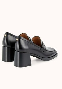 Chaussures noires en cuir à talons avec une finition lisse, des talons carrés angulaires et des détails tissés sur le devant. L'intérieur présente une doublure marron.