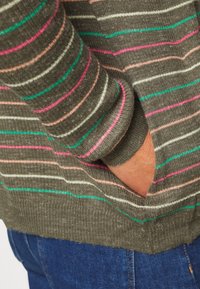 Sweter w paski w oliwkowej zieleni z różowymi, turkusowymi i białymi poziomymi liniami. Posiada ściągacze na mankietach i kieszeń z przodu. Miękka dziana tekstura.