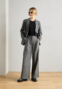 Grå rutmönstrad blazer och grå högmidjade byxor, båda med skräddarsydd passform. Svart topp och svarta skor med grov sula fulländar looken.