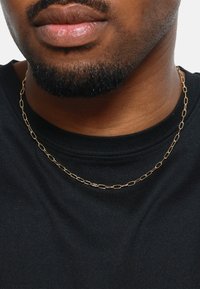 Collar de cadena de oro con eslabones ovalados, descansando sobre una camiseta negra. El fondo es completamente blanco, resaltando el diseño de la joyería.