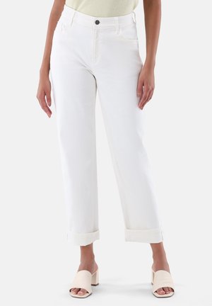 Weiße Denim-Hosen mit umgeschlagenen Säumen, ausgestattet mit einem Knopfverschluss und Fronttaschen, kombiniert mit nudefarbenen Blockabsatzsandalen.