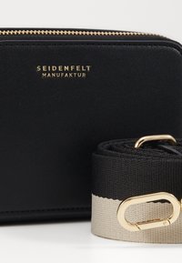 Borsa in pelle nera con accessori dorati e logo impresso. Include una tracolla nera e crema con un gancio dorato. Finitura testurizzata e chiusura con zip.
