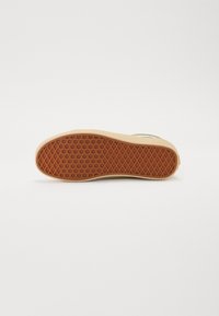 Semelle extérieure de chaussure avec un motif en caoutchouc brun texturé, présentant un design en nid d'abeille. Semelle intermédiaire beige doux visible sur les bords.