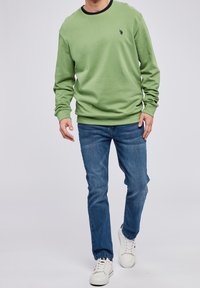 Vihreä huppari pyöreällä kaula-aukolla ja ribbireunuksilla, yhdistettynä sinisiin farkkuihin ja valkoisiin lenkkareihin. Rentoa tyyliä, yksinkertainen muotoilu ja tekstuuri.