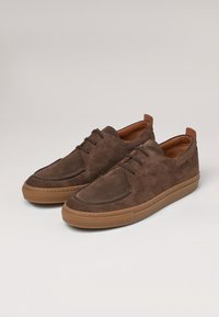 Baskets en daim marron avec un embout lisse, semelle en caoutchouc beige contrastant et couture discrète. Comprend trois œillets et un onglet à l'arrière.