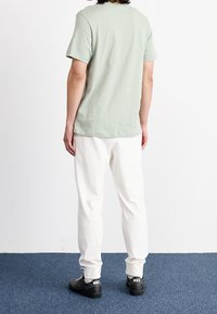 Jasnozielona bawełniana koszulka, krótki rękaw, okrągły dekolt; w zestawieniu z białymi spodniami dresowymi. Czarne sneakersy z białym logo; jednolite tło.