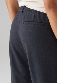 Marinblå herringbone-mönstrade byxor med en bakficka och elastisk midja, som visar en texturerad tyg och skräddarsydd design.