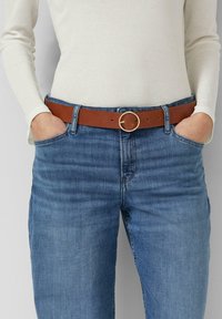 Brązowy skórzany pasek z okrągłą złotą klamrą, noszony na niebieskich dżinsach, charakteryzujący się gładką fakturą i klasycznym designem.