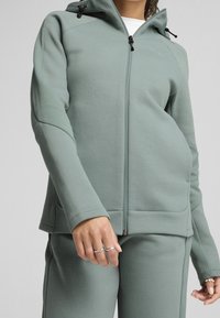 Lichtgroene hoodie met ritssluiting en capuchon, met gestructureerde accenten op de mouwen en voorzakken. Gemaakt van zacht materiaal, gecombineerd met bijpassende broek.