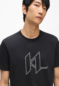 Melna T-kreklis ar īsām piedurknēm, apaļu kakla izgriezumu, ar baltu studēta logotipu priekšpusē. Gluda auduma, ar parasto piegriezumu.