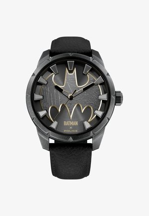 Juodos odos dirželio laikrodis su tekstūruotu tamsiai pilku ciferblatu, kuriame dominuoja ryškus Batmano logotipas ir aukso spalvos akcentai, taip pat kampuoti valandų žymekliai.