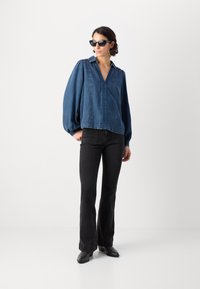 Denimbluse med puffede ærmer, dyb v-hals, indviklet syning ned ad forsiden, parret med sorte flared jeans og sorte ankelstøvler.