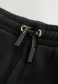 Pantalones atléticos negros con una cintura elástica, que presentan una tela texturizada, ojetes de acento dorado y un cordón negro con detalles de logotipo.