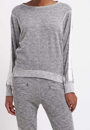 Personne portant un haut à manches longues gris et un pantalon assorti avec des détails de bandes blanches et des poches zippées sur le pantalon.