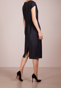 Námořnické šaty s výstřihem a krátkými rukávy, se zadním rozparkem a skrytým zipem vzadu, doplněné černými lodičkami na vysokém podpatku.