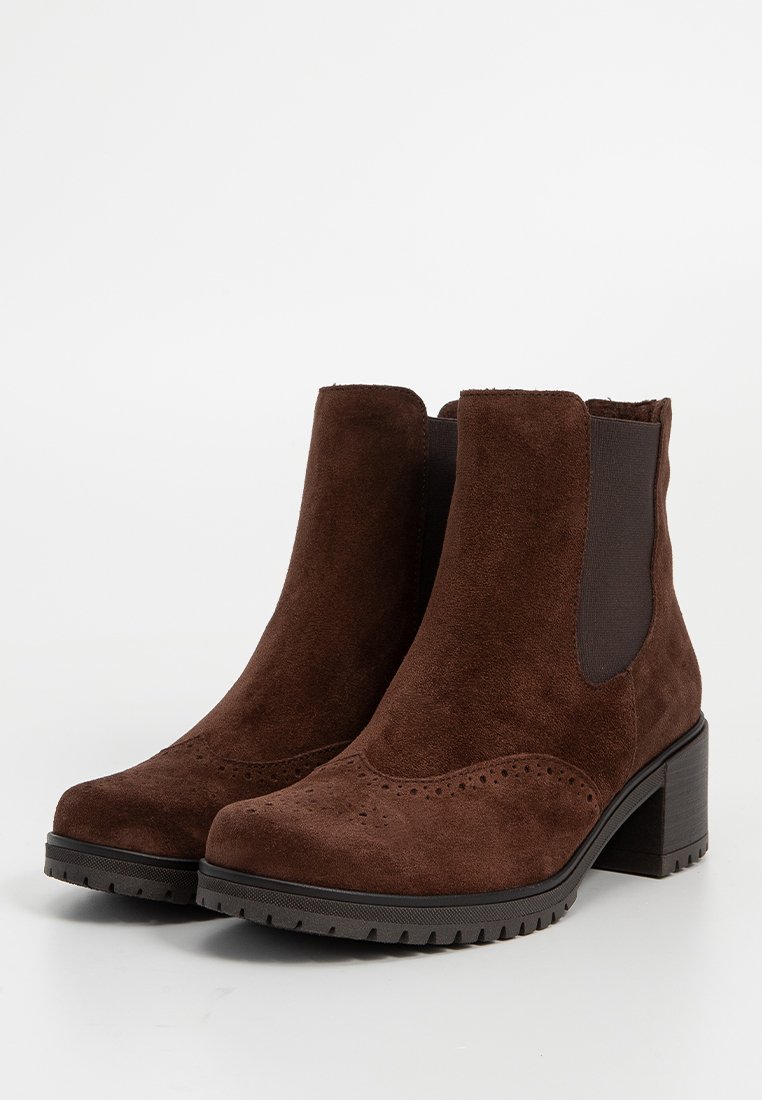 Un par de botas de tobillo de ante marrón con paneles laterales elásticos, perforaciones decorativas, tacones gruesos y suelas de goma negra con relieve.