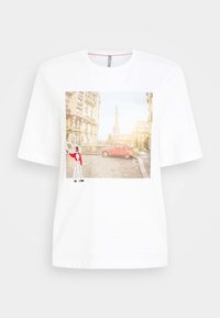 Vit T-shirt med en rektangulär tryck som föreställer en parisk gatuscen, en röd bil och Eiffeltornet. Inkluderar en broderad figur i rött och vitt.